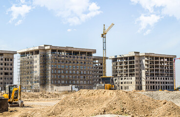 High-rise buildings under construction in scaffolding against the background of the sky.Construction site. Construction cranes and high-rise building under construction against blue sky. © kvdkz