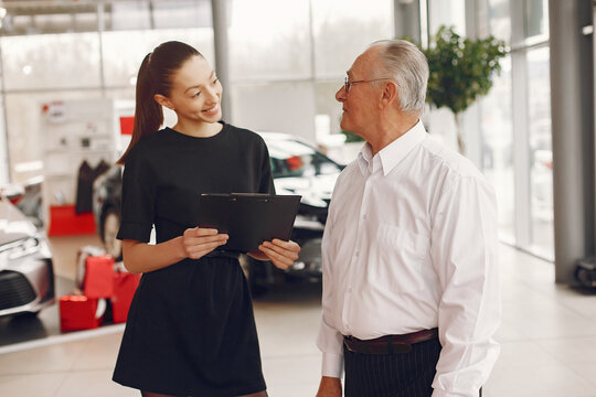 Senior in a car salon. Old man buying the car. Elegant woman helps a man buy a car.
