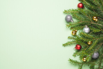 Green spruce branches with christmas balls decorations on pastel green color background. Flat lay on plain background