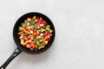 Frying pan with sliced frozen vegetables mix on a white background. Copy space, view from above.