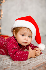 Cute baby Santa sits at home near the Christmas tree with gifts