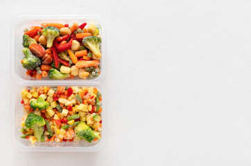 Frozen sliced vegetables salad in plastic containers on a white background. Copy space, view from above.