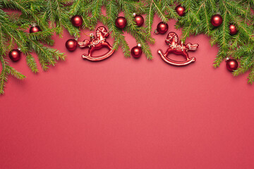 Christmas tree branches and sparkling toys on red plain background. Christmas and New Year holidays greeting card, copy space, top view