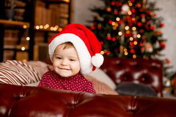 Cute baby Santa sits at home near the Christmas tree with gifts