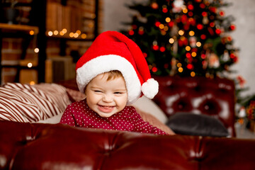 Fototapeta na wymiar Cute baby Santa sits at home near the Christmas tree with gifts