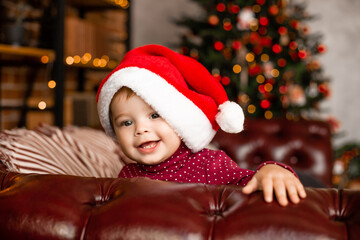 Cute baby Santa sits at home near the Christmas tree with gifts