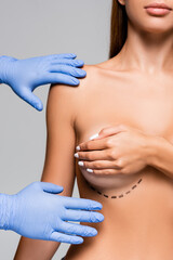 Cropped view of plastic surgeon in latex gloves touching naked woman with marks on breast isolated...