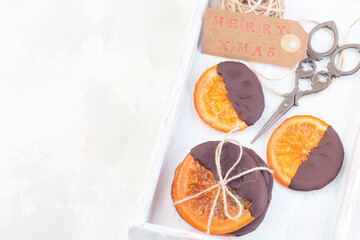 Homemade candied sliced oranges covered with chocolate on white tray, horizontal, copy space, top view
