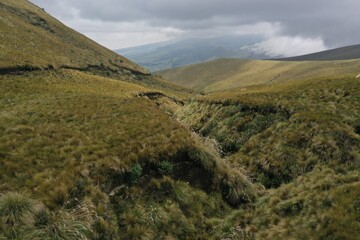 Aerial view of a hill following a dry riverbed in the Andes of Ecuador covered by dry green and yellow grass