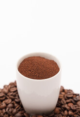 white ceramic cup with coffee powder inside, with coffee beans and white background