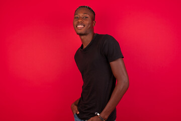 Portrait of successful Young African American handsome man standing against red background, smiling broadly with self-assured expression. Confidence and business concept.