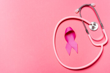 Top view of stethoscope and symbol of breast cancer awareness on pink surface