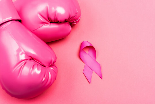 Top view of boxing gloves and ribbon of breast cancer awareness on pink surface