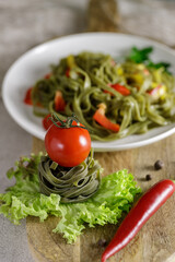 Raw spinach tagliatelle pasta with cherry tomato and vegetables on wooden board. Selective focus