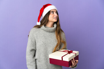 Girl with christmas hat holding a present isolated on white background thinking an idea while looking up