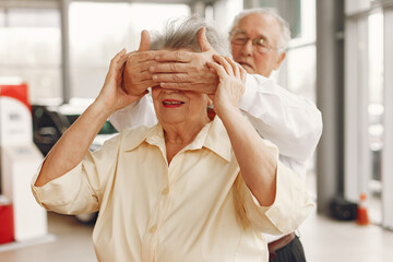 Old couple in a car salon. Family buying the car. Elegant woman with her husband. Senior by a car.