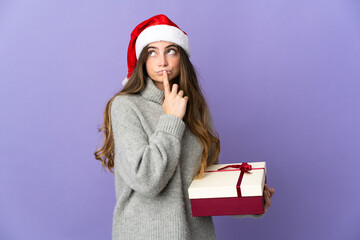 Girl with christmas hat holding a present isolated on white background having doubts while looking up