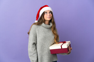 Girl with christmas hat holding a present isolated on white background and looking up