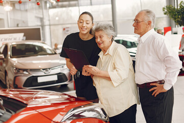 Senior in a car salon. Old couple buying the car. Elegant woman helps a old people buy a car.