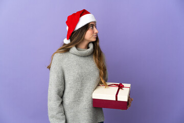 Girl with christmas hat holding a present isolated on white background looking to the side