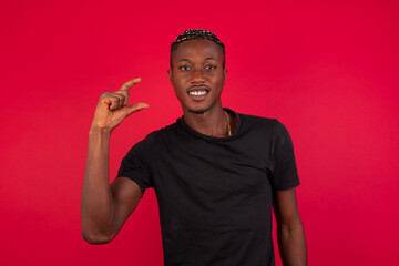 Young African American handsome man standing against red background smiling and gesturing with hand small size, measure symbol.