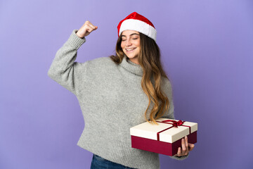 Girl with christmas hat holding a present isolated on white background doing strong gesture
