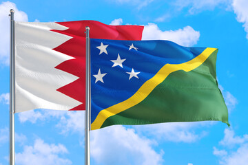 Solomon Islands and Bahrain national flag waving in the windy deep blue sky. Diplomacy and...