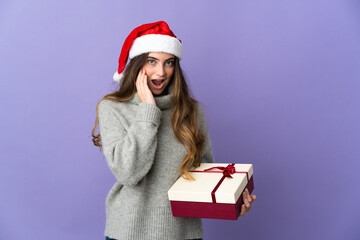 Girl with christmas hat holding a present isolated on white background with surprise and shocked facial expression