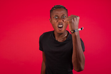 Fierce Young African American handsome man standing against red background holding fist in front as if is ready for fight or challenge, screaming and having aggressive expression on face.