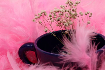 Small and white wildflowers in indigo blue teacup, pink feather textured background, peace and...