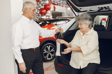 Old couple in a car salon. Family buying the car. Elegant woman with her husband. Senior by a car.