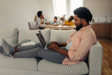 Black man with earphones sitting on the floor and using laptop