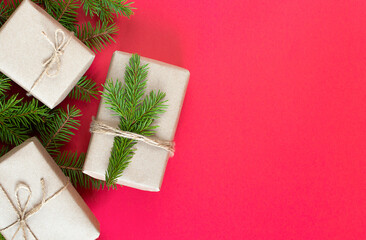 Fototapeta na wymiar Christmas gifts in craft paper and a fir branch on red background. zero waste packaging for gifts