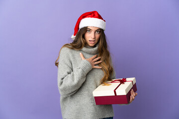 Girl with christmas hat holding a present isolated on white background surprised and shocked while looking right