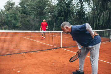 Obraz premium middle aged man having backache injury on tennis court