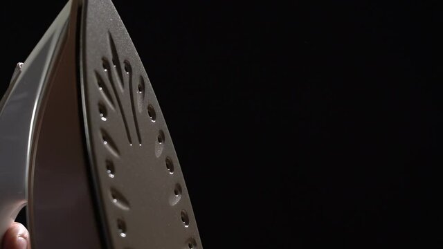 The iron is releasing steam on a black background. Close-up. Household electrical appliances concept.