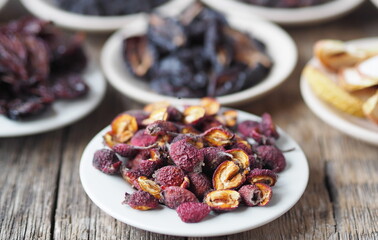 Dried hawthorn on the foreground. Background with bowls with various dried fruits on a wooden ancient background. Home preparation of dried fruits.
