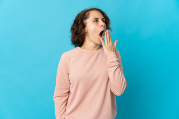 Young English woman isolated on blue background yawning and covering wide open mouth with hand