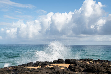Surf sprays up over the top of lava rocks on a Kauai beach