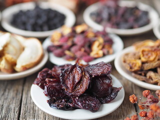 Dried prunes on the foreground.Background with bowls with various dried fruits on a wooden ancient background. Home preparation of dried fruits.