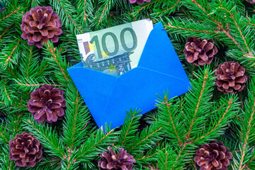 A banknote of 100 euros in a blue envelope against the background of Christmas tree branches. Concepts of expensive gifts for the New Year.