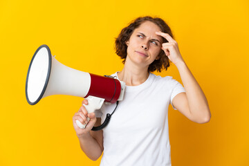 Young English woman isolated on yellow background holding a megaphone and having doubts