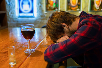 Alcoholism concept. A young man sits alone at the bar in a pub. Social problem. Fight against alcohol addiction, crisis, depression.