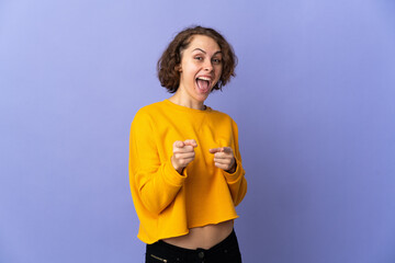 Young English woman isolated on purple background surprised and pointing front