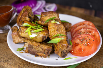 Grilled fat pork ribs on a bone served on a plate with vegetables. Roasted barbeque meat on dark background.