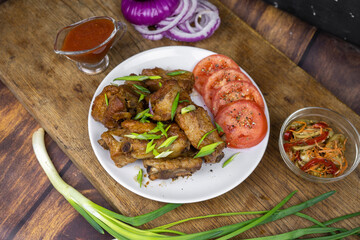 Grilled fat pork ribs on a bone served on a plate with vegetables. Roasted barbeque meat on dark background.