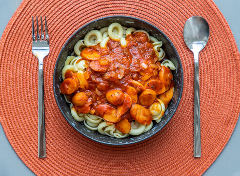 Dischi pasta with sausage, onion and balognese sauce in a black plate on red background. Copy space, No focus, specifically.