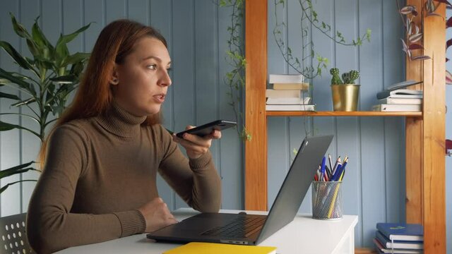 Businesswoman sitting at workplace desk hold smartphone call up with colleague on speakerphone, solve work-related issues, leave voicemail response