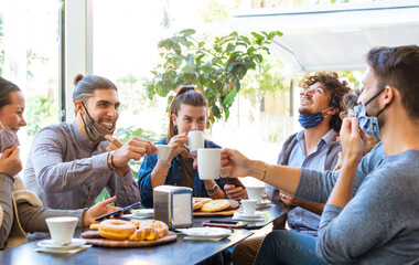 group students having fun drinking coffee at coffeehouse wearing protective face mask. young friends talking together at restaurant cafeteria. New normal lifestyle concept with happy guys and girls 