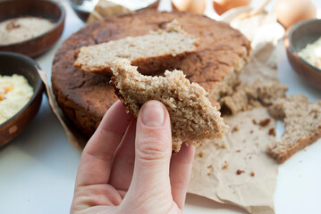 Round gluten-free homemade bread from buckwheat, chickpea, rice, cornmeal, eggs and honey. Healthy eating concept, flat lay. A piece of bread in a female hand.